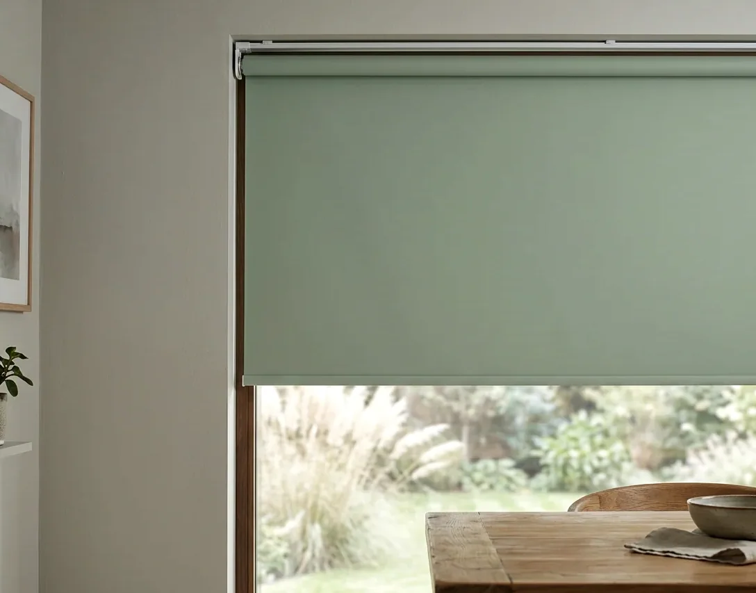 Roller blind lowered over a garden-facing window — one smooth fabric panel on a tube, with no folds or slats