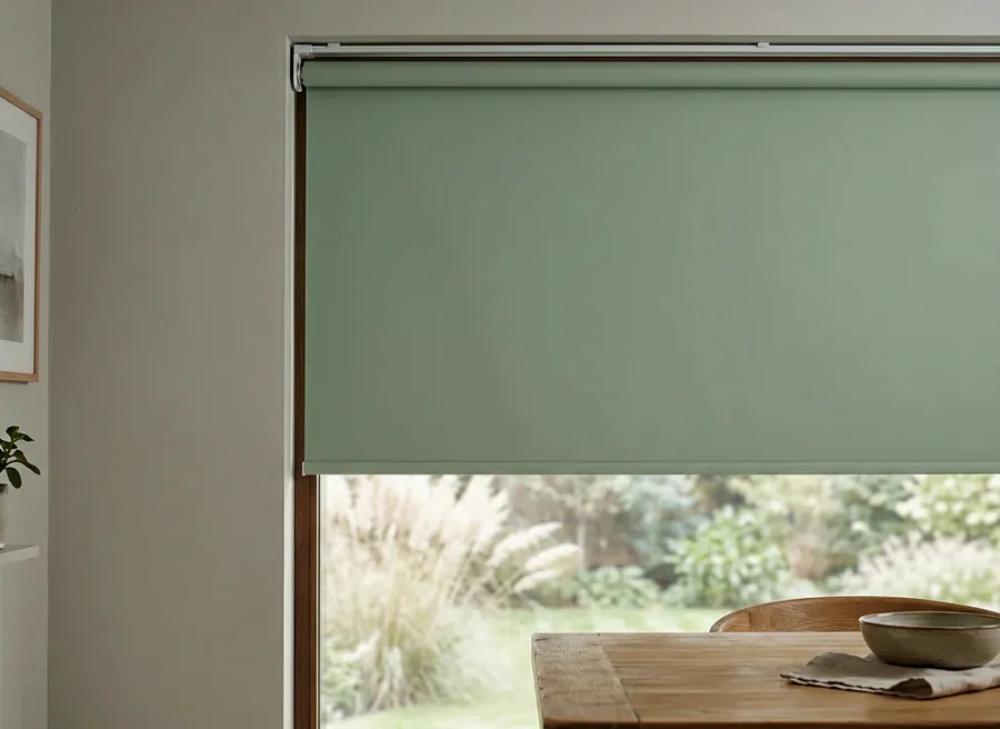Sage roller blind — one smooth fabric panel on a tube — lowered over a garden-facing window in a Kyalami home
